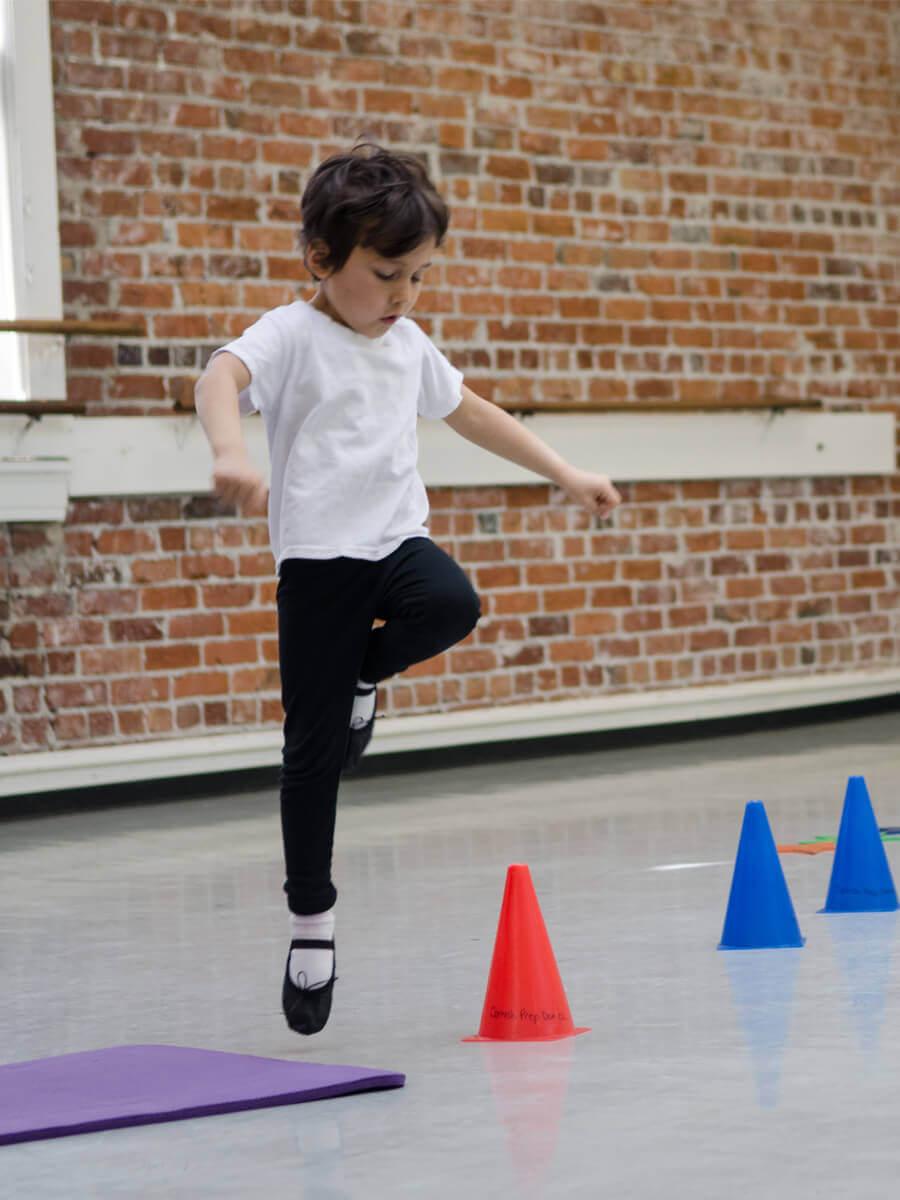 A young male dancer doing a movement exercise around traffic cones in a dance studio