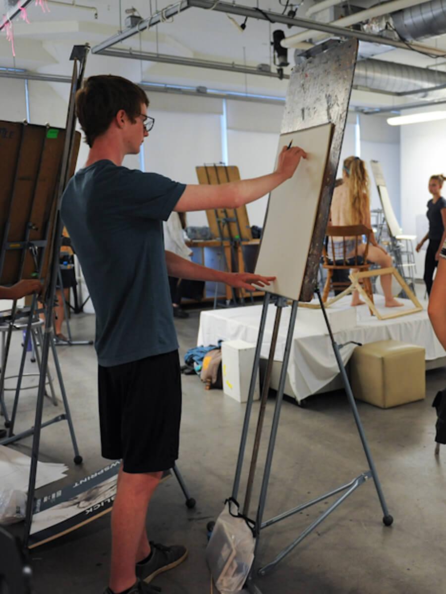 students in art studio with easels drawing live model