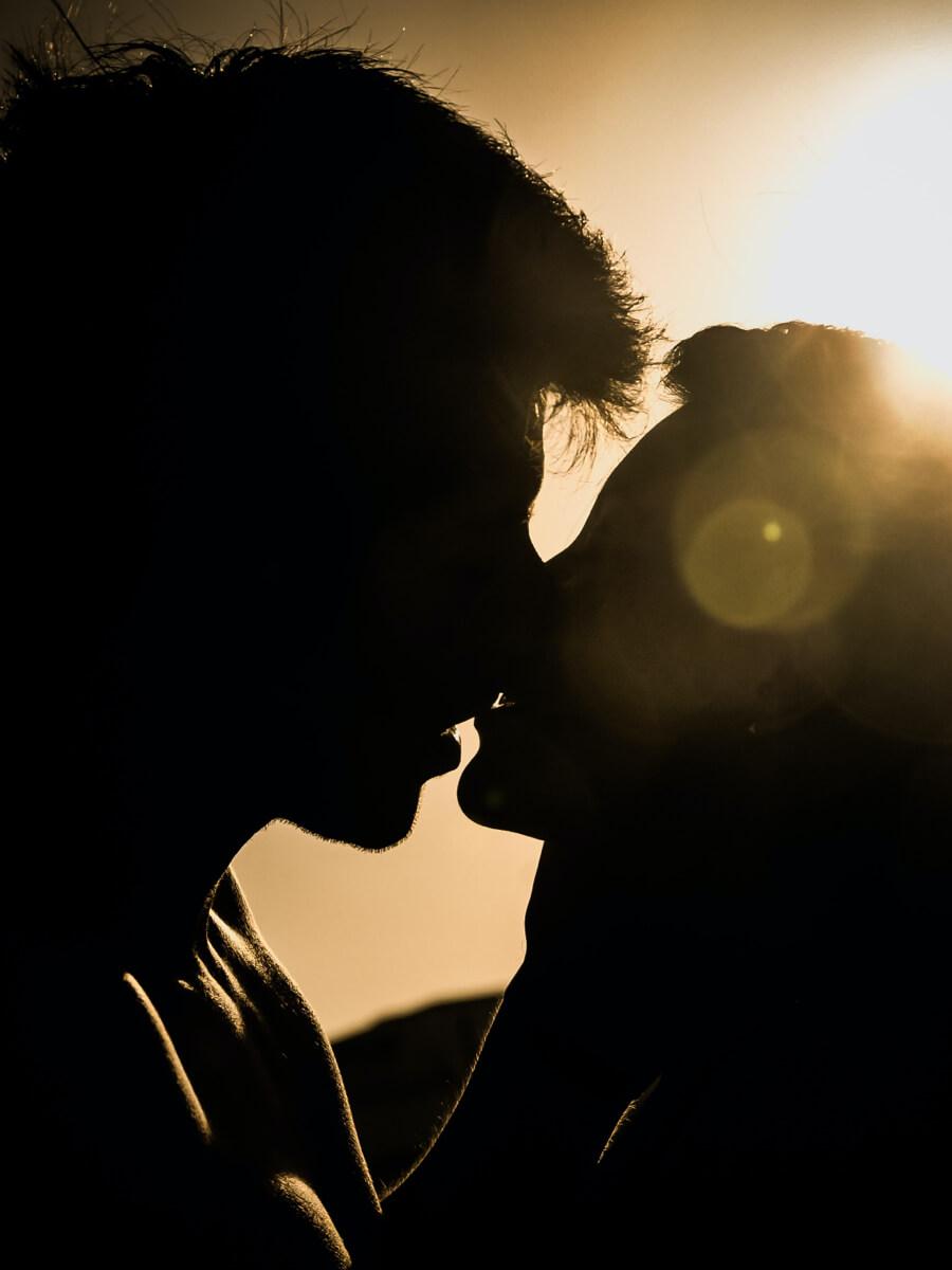 Man and woman kissing, with a light behind them so they look silhouetted