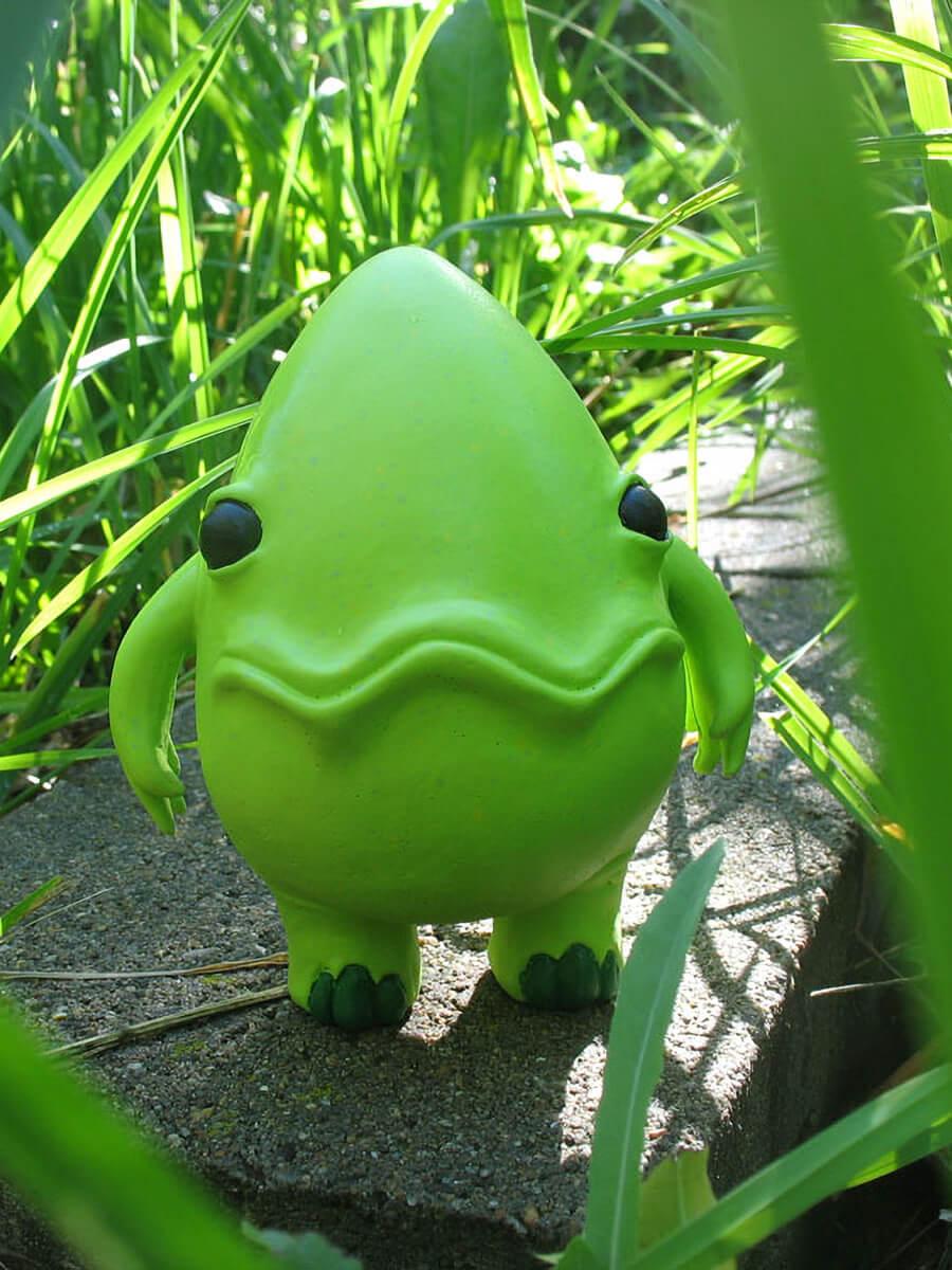 Green egg shaped figurine with two arms, legs and a wavy smile. 