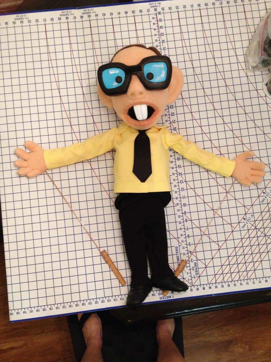 Stop motion pupped with glasses and buck teeth with a yellow shirt and black tie.