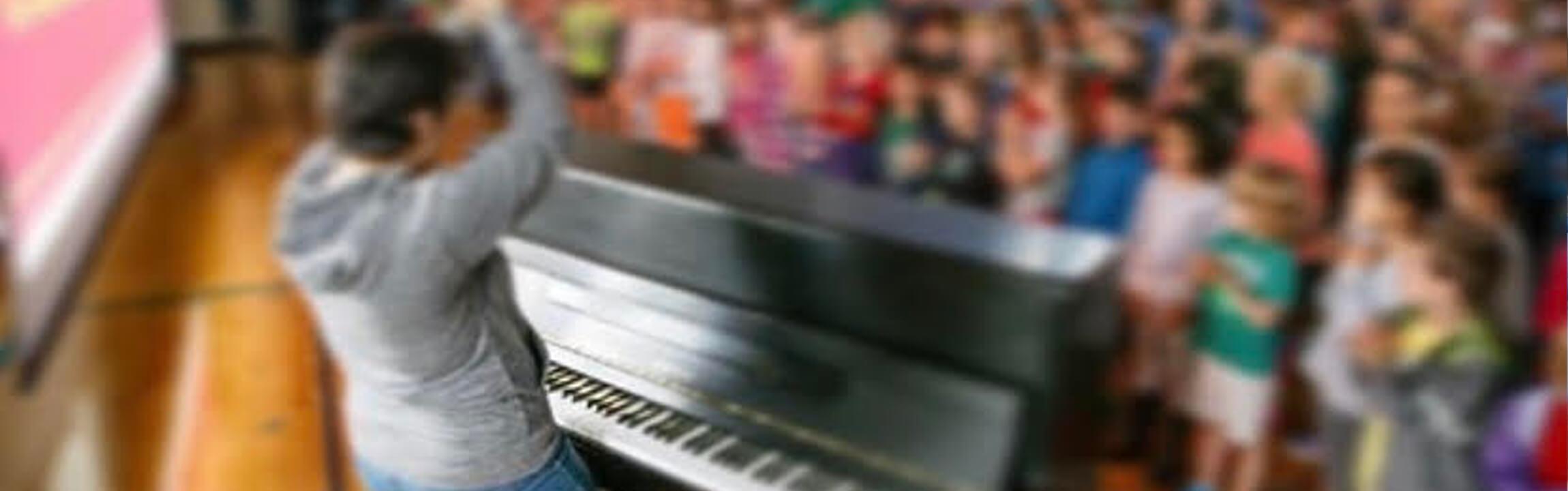 Choir conductor in front of a piano and children's choir.