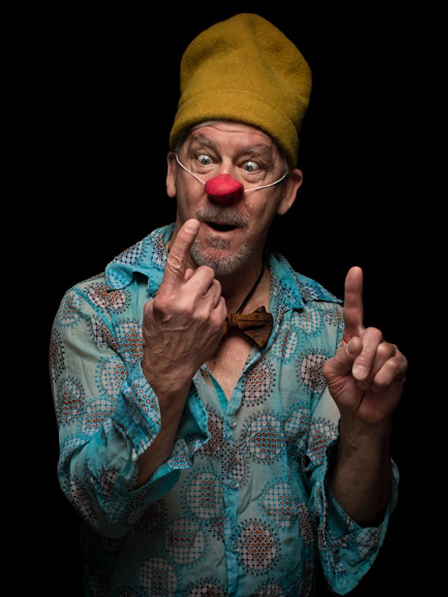 clown nose actor with black background and yellow hat blue shirt