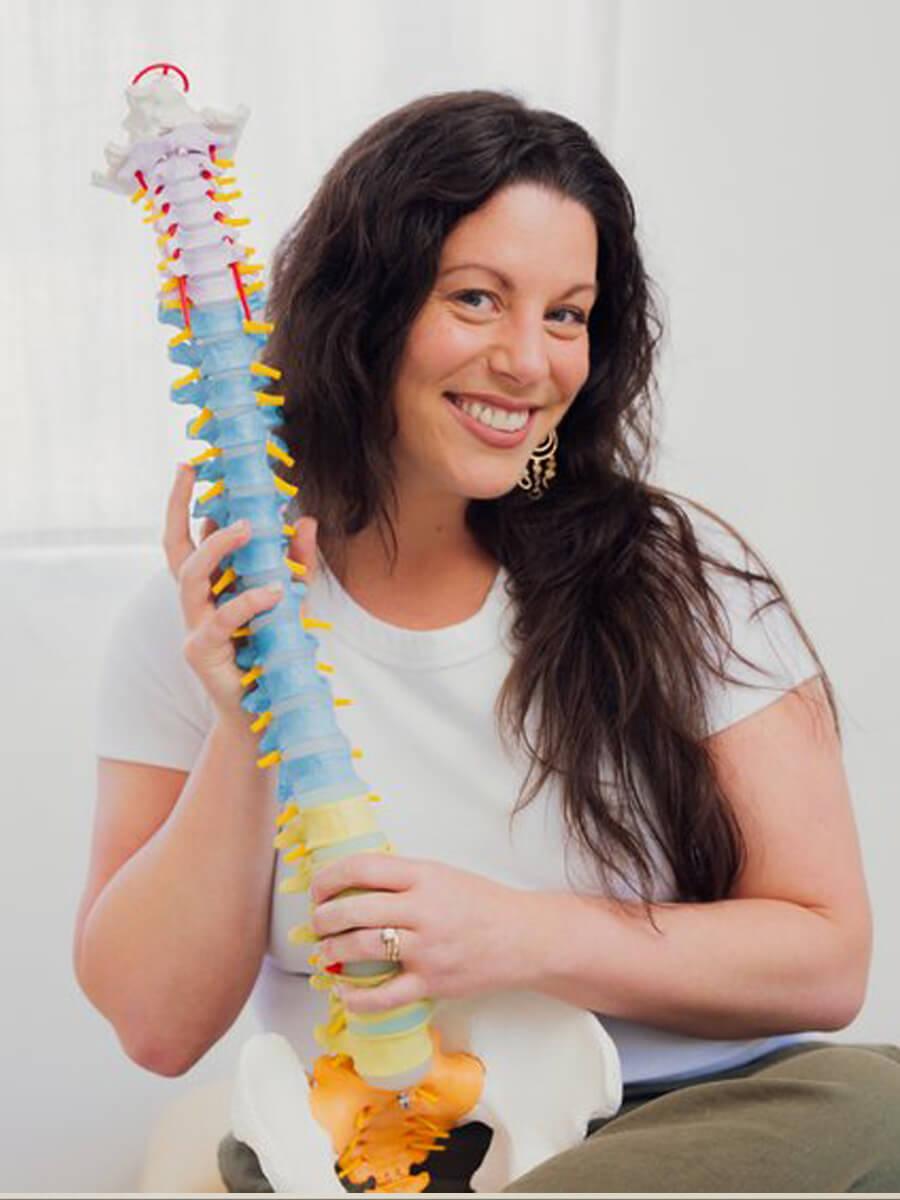 Jenna Spinei holding a model of a spine, brown hair white tee shirt. 