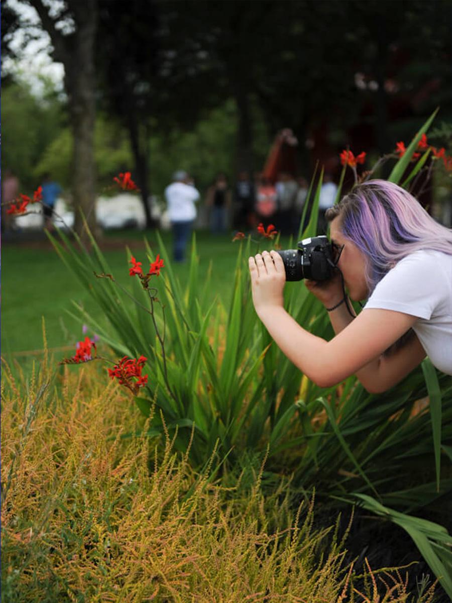 Girl with purple hair taking a photo of flowers