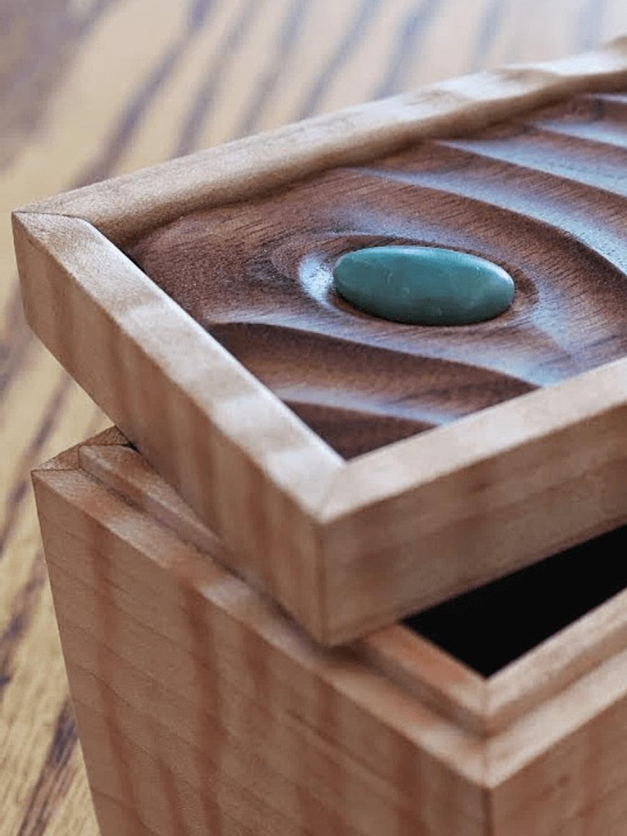 Wooden box with a jade stone on top, light wood box with a dark wood top. 