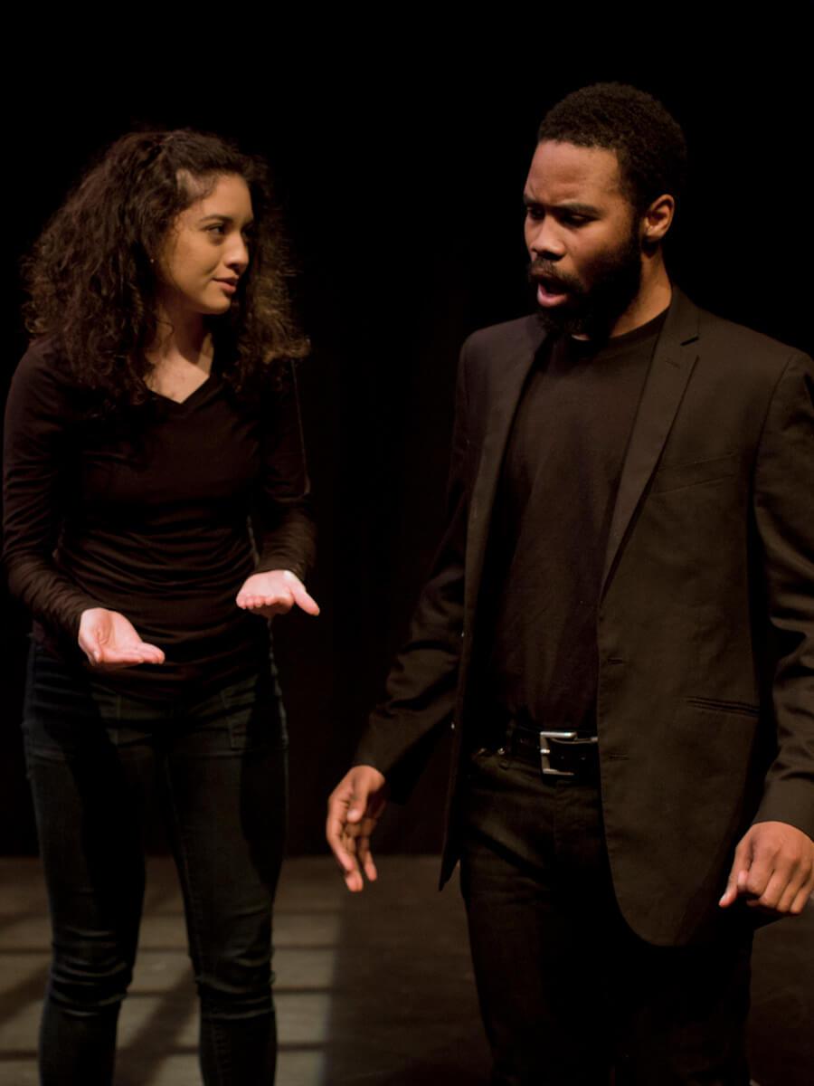 2 actors wearing all black on stage acting as though they are in an argument. 