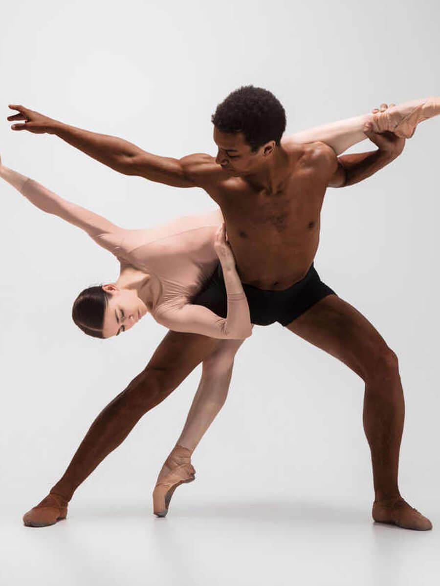 Two dancers in a pose together one is a black male and the other bent over them is a white woman or person.