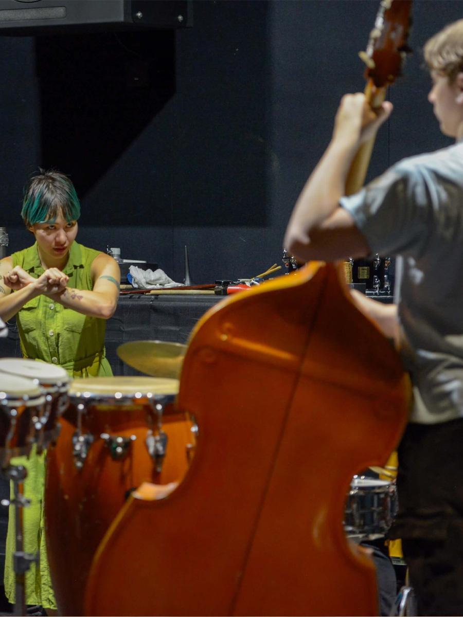 Musicians on stage with bass up front and the instructor directing the bass player.