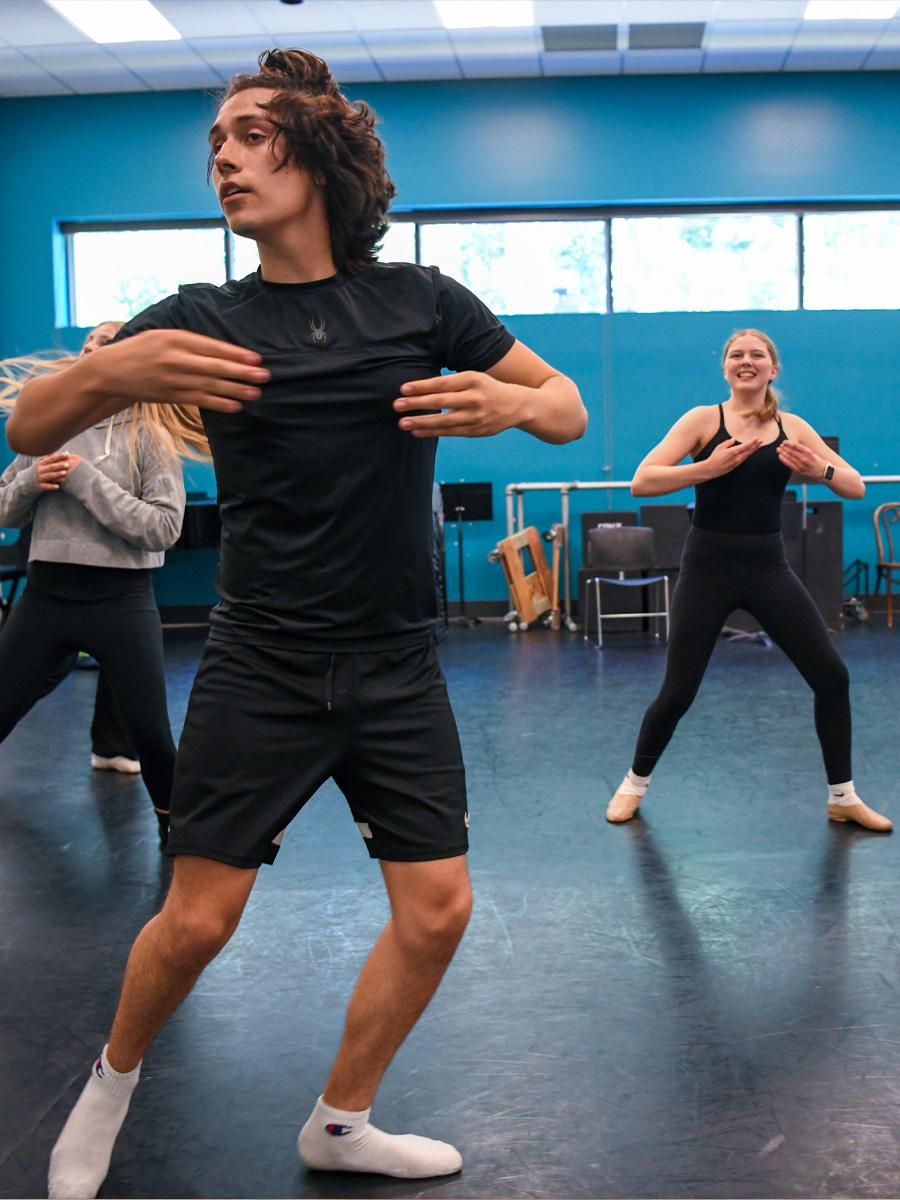Students in a movement studio in black practicing dance for musical theater with blue walls