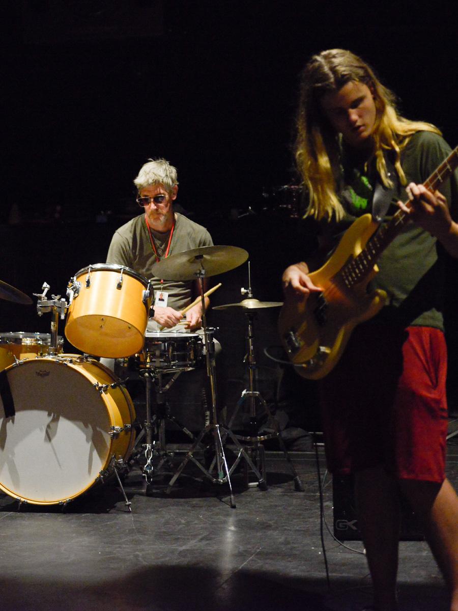 Students on stage playing music drums and electric bass