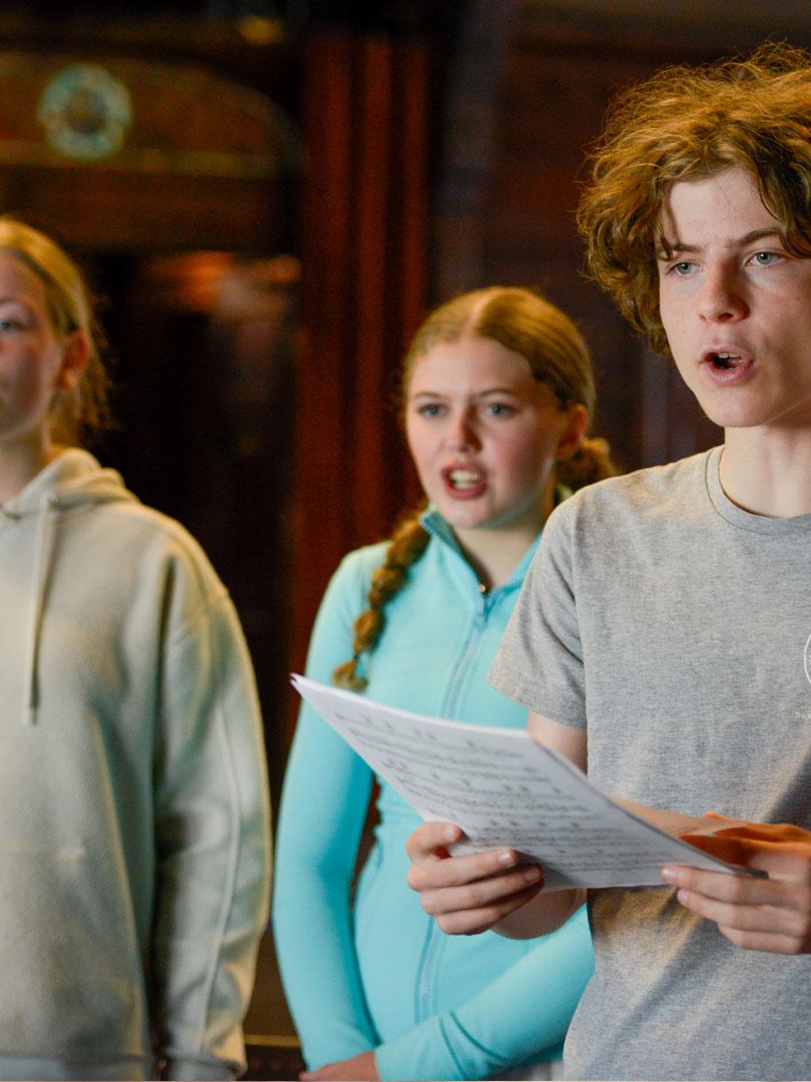 three singers on stage practicing music with sheet music singing. 