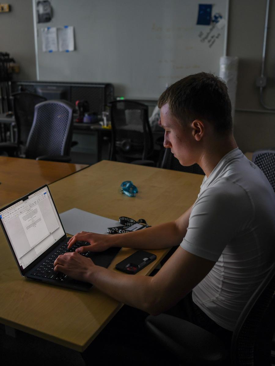 Students reading from a projector in a dark room and large table writing on laptops
