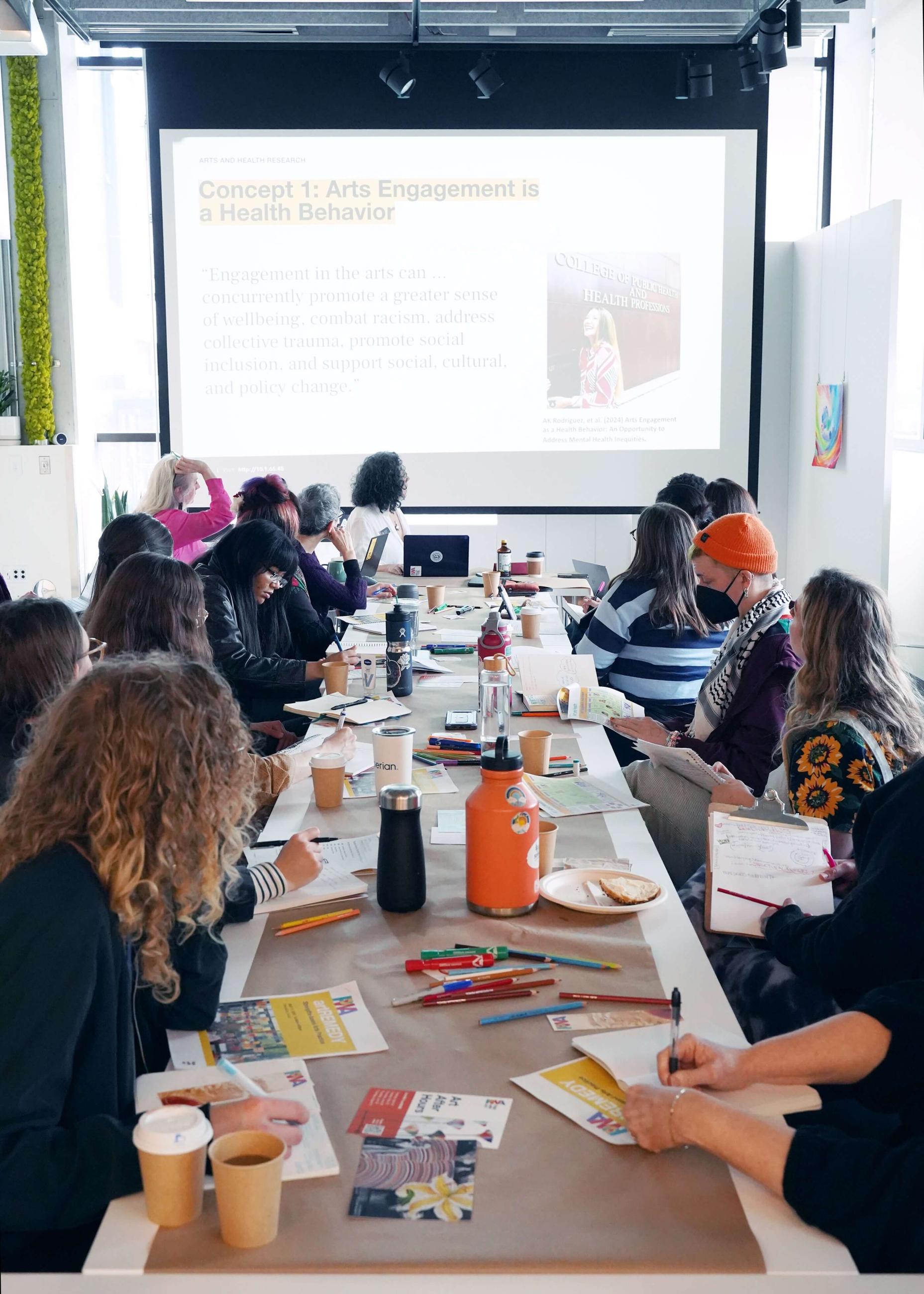 Art students around a long table discussing ideas all dressed in fall colors or hats.