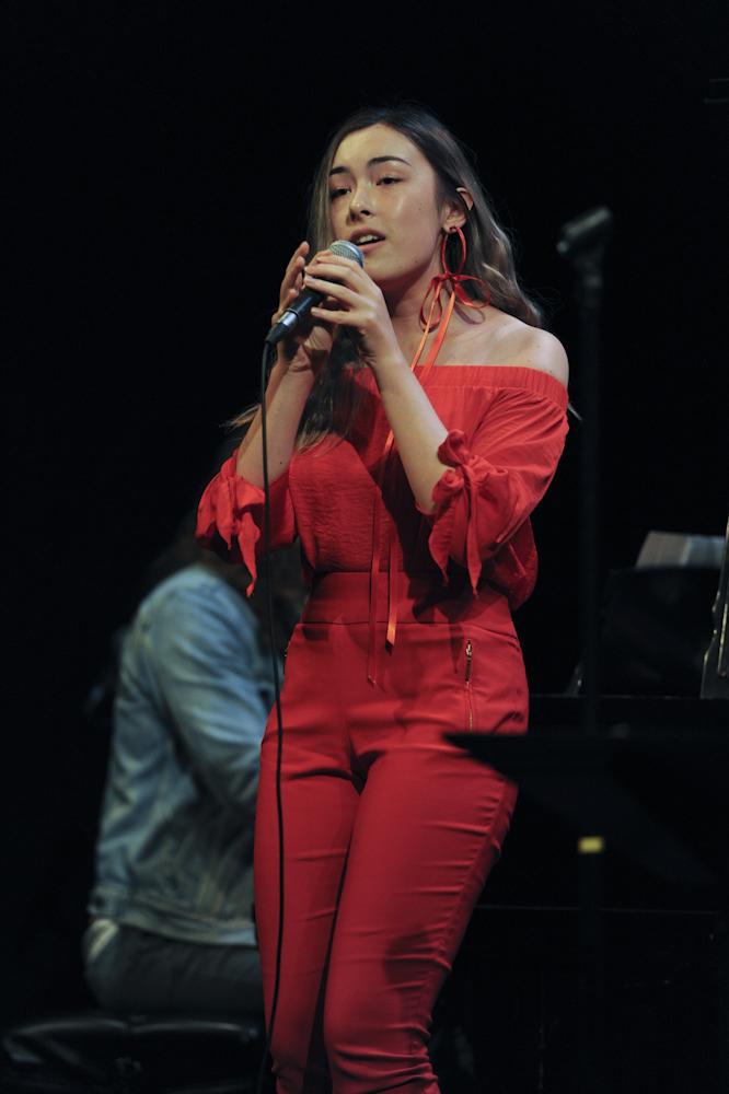 Voice student singing on stage with a student band all wearing red.
