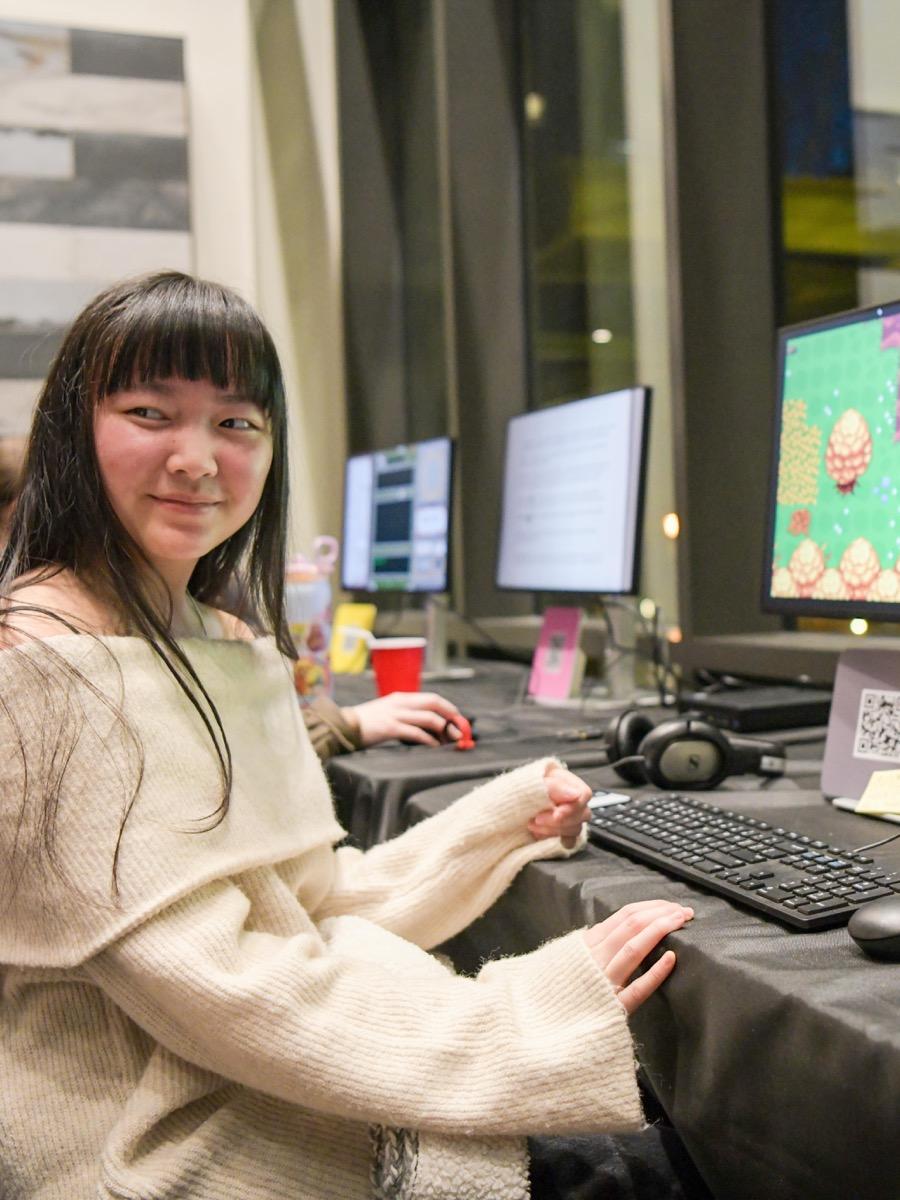 Girl in a white sweater sitting at a computer with motion graphics smiling