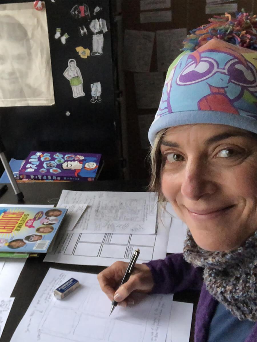 white woman wearing funny hat smiling into camera with pencil in hand and eraser nearby