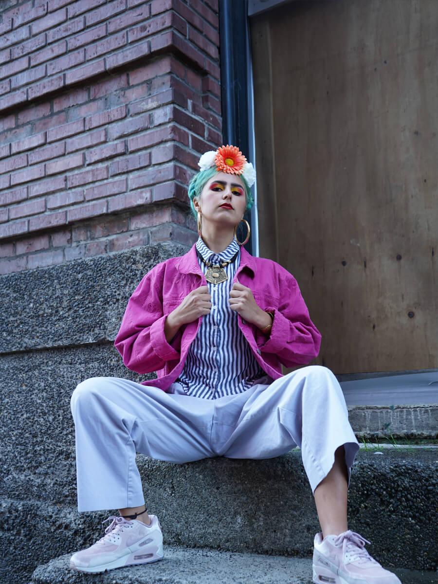 queer person of color wearing pink jacket looking into camera