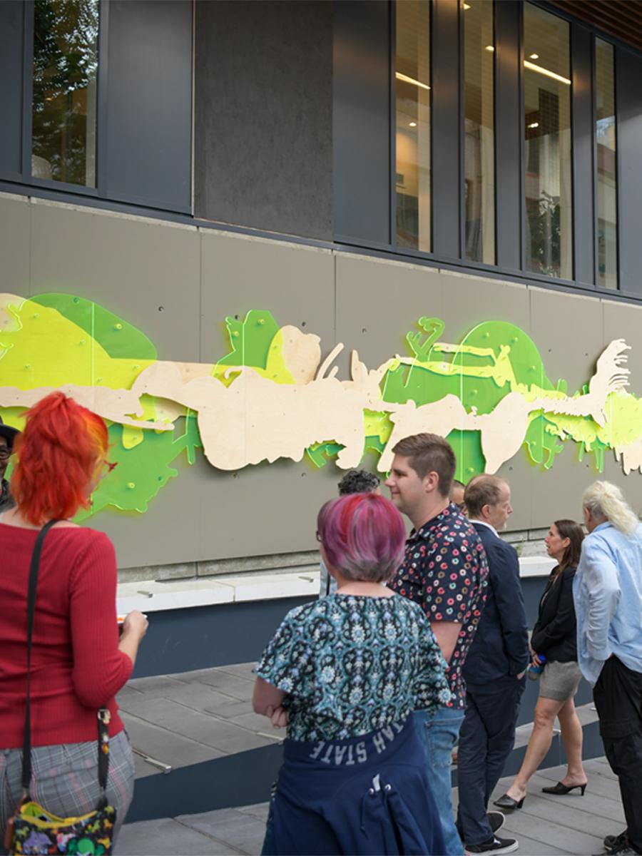 people standing outside by neon green mural titled Cut Crush Decay