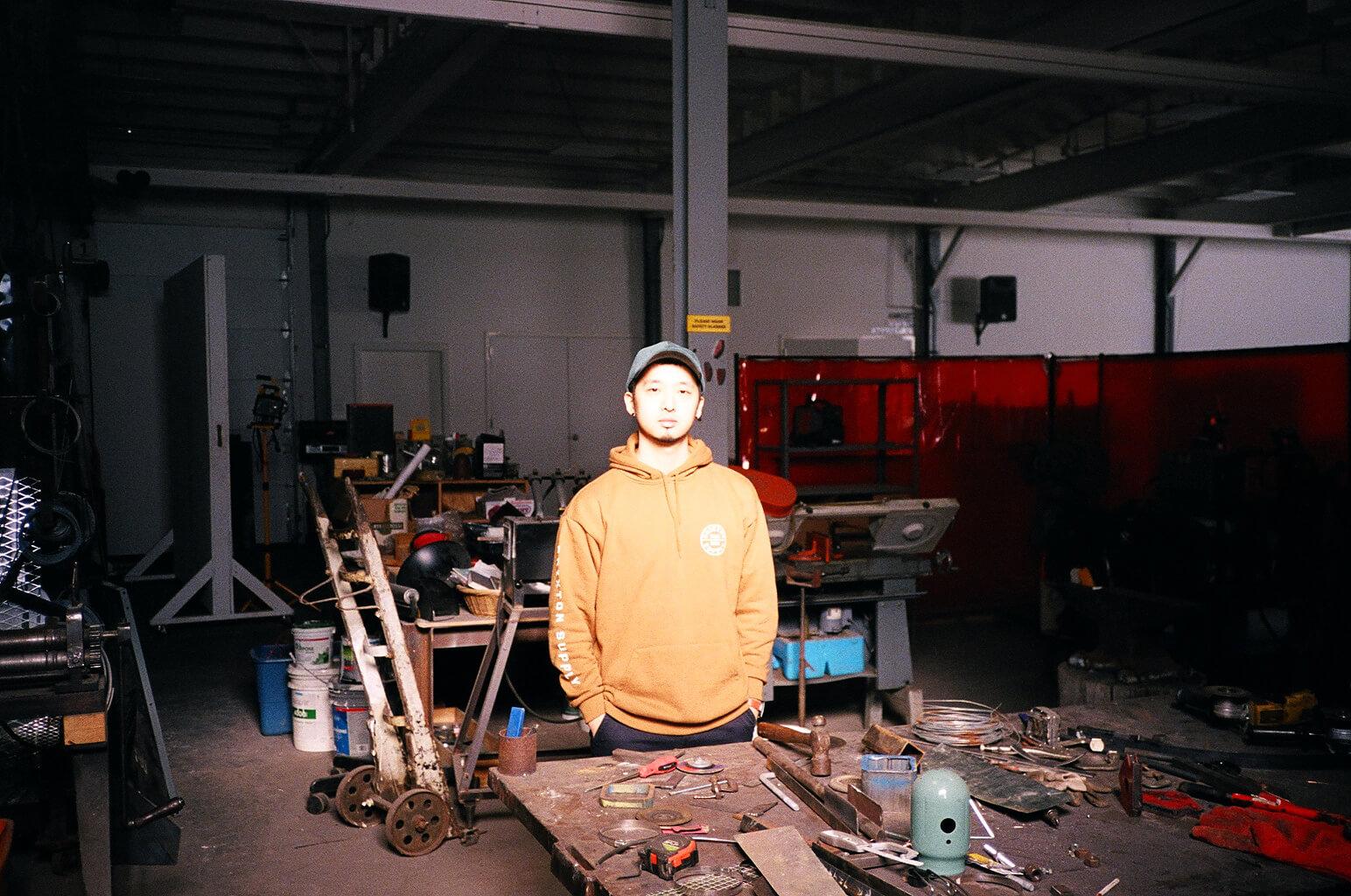 Kyungjin Kim standing in a yellow hoodie in a metal shop. 