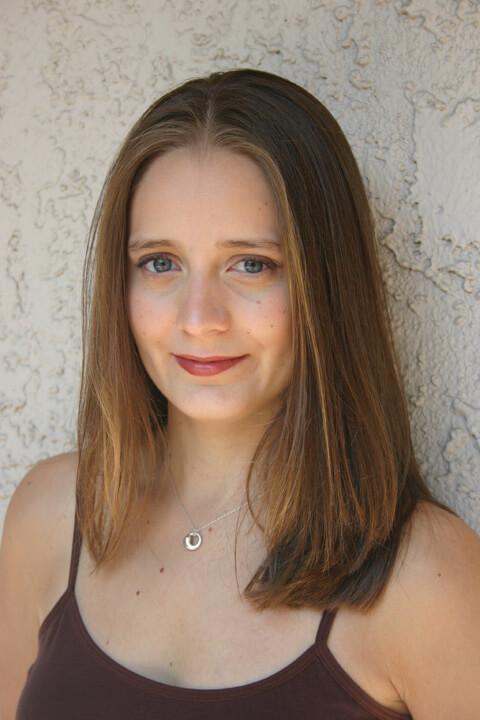 Nikki Rice with a brown tank top shoulder brown hair against a white wall.
