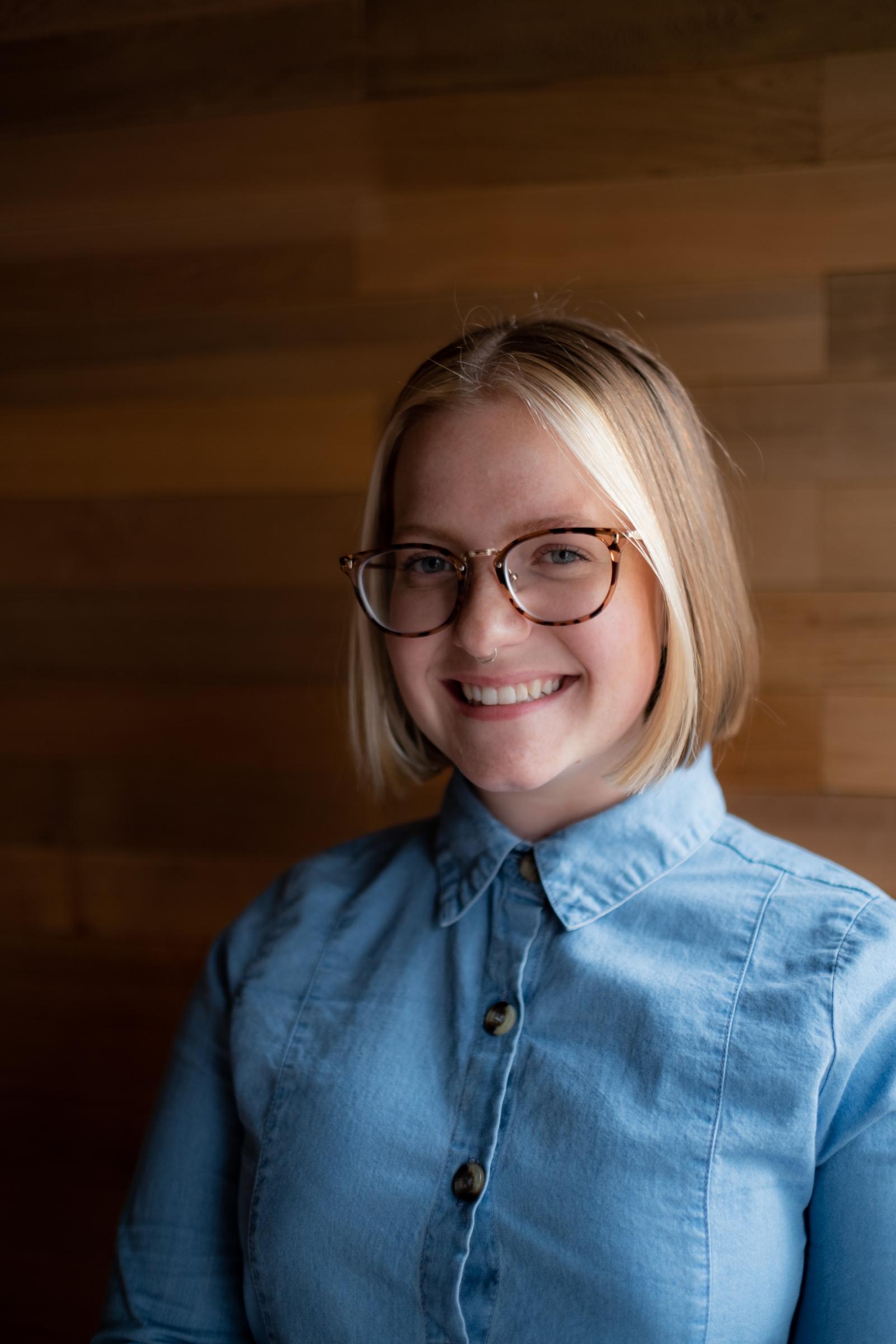 Zoe Crago with a blue denim shirt on and brown glasses. 