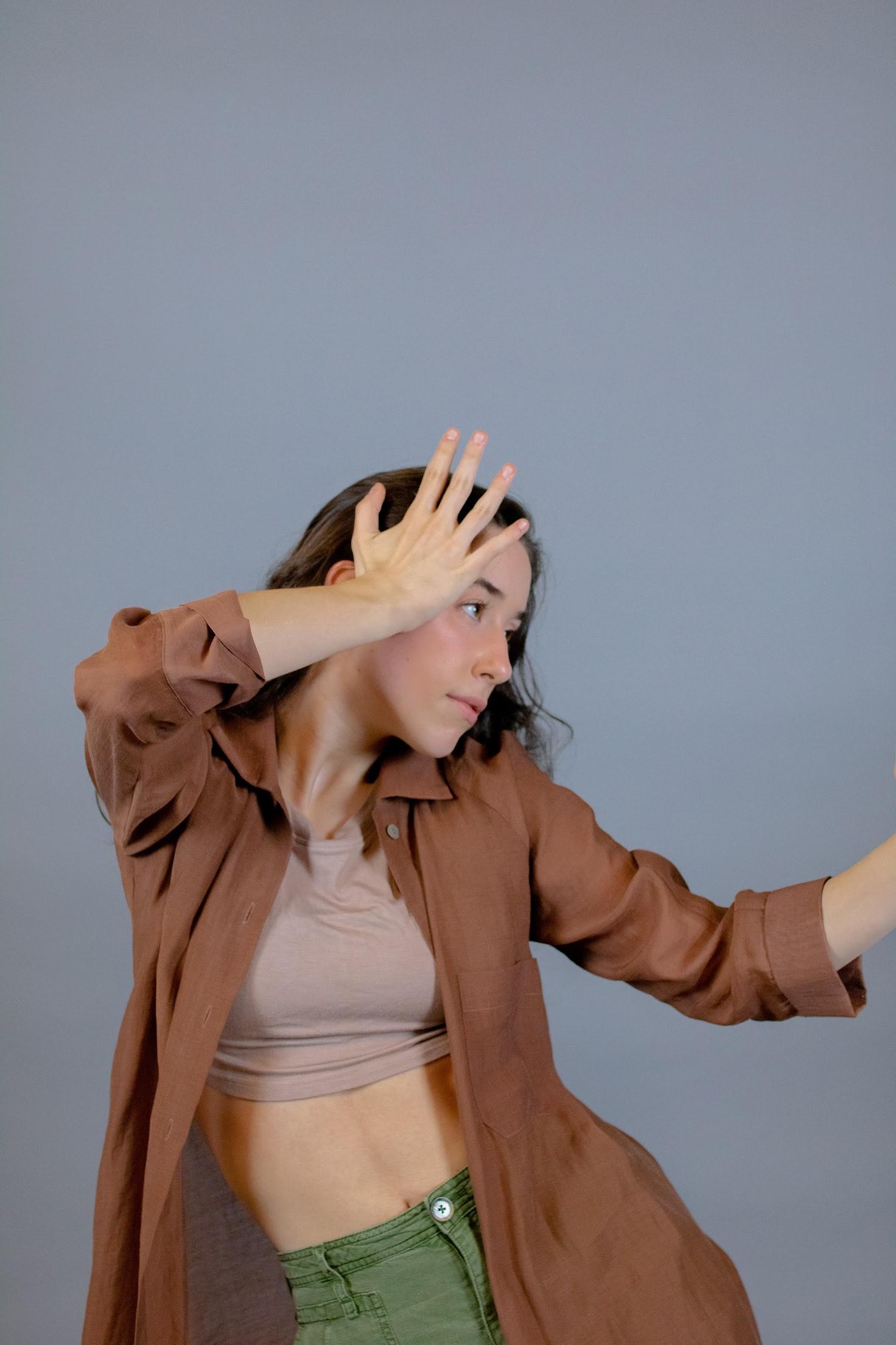 Olivia Anderson in a brown shirt with green pants in a dance pose. 