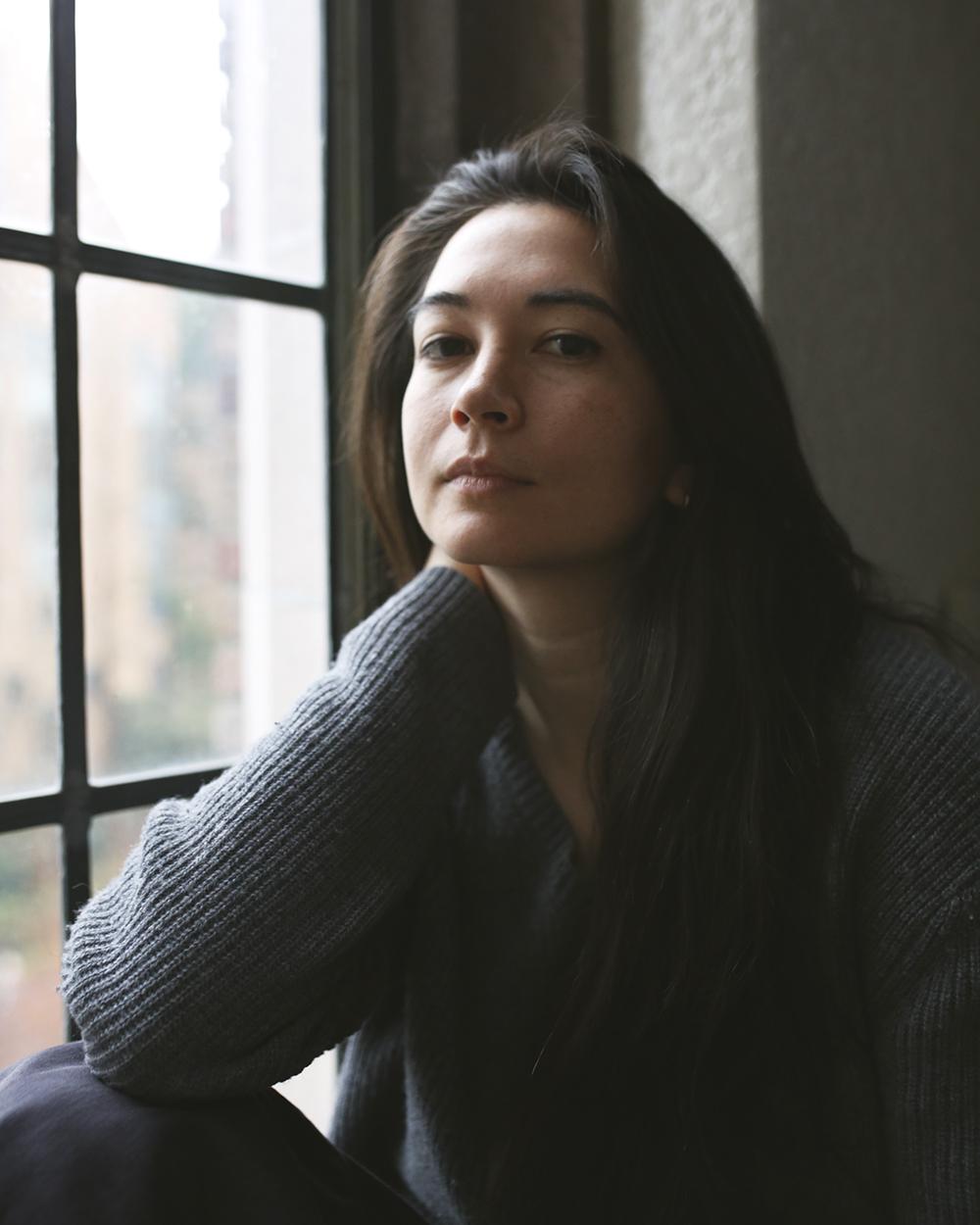 Cameo Lethem in a grey shirt with long brown hair sitting next to a window.