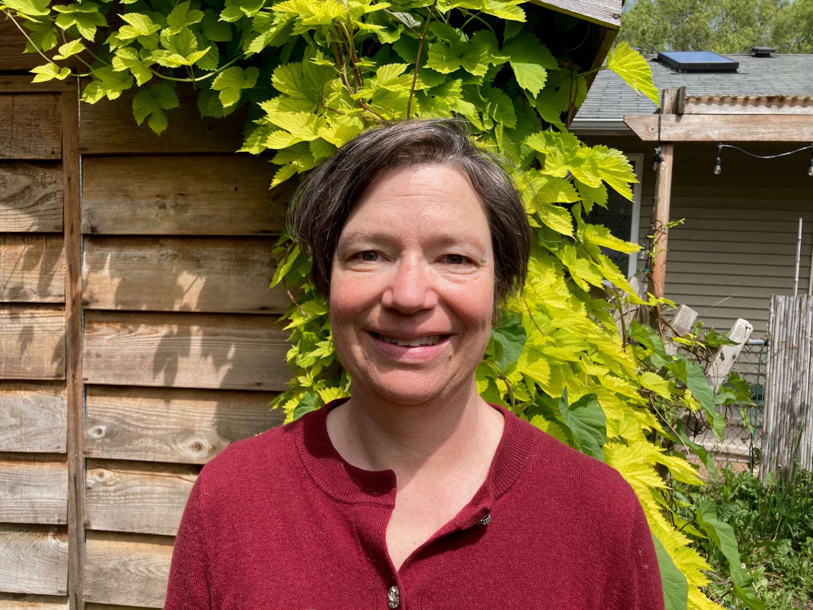 Megan Kelso in a red shirt short hair with a vine behind her. 