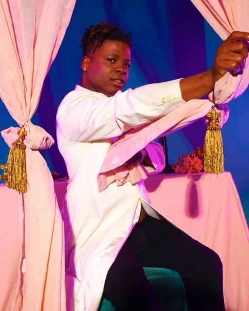 Keyes Wiley in a white shirt and blue back ground holding a pink stage curtain.