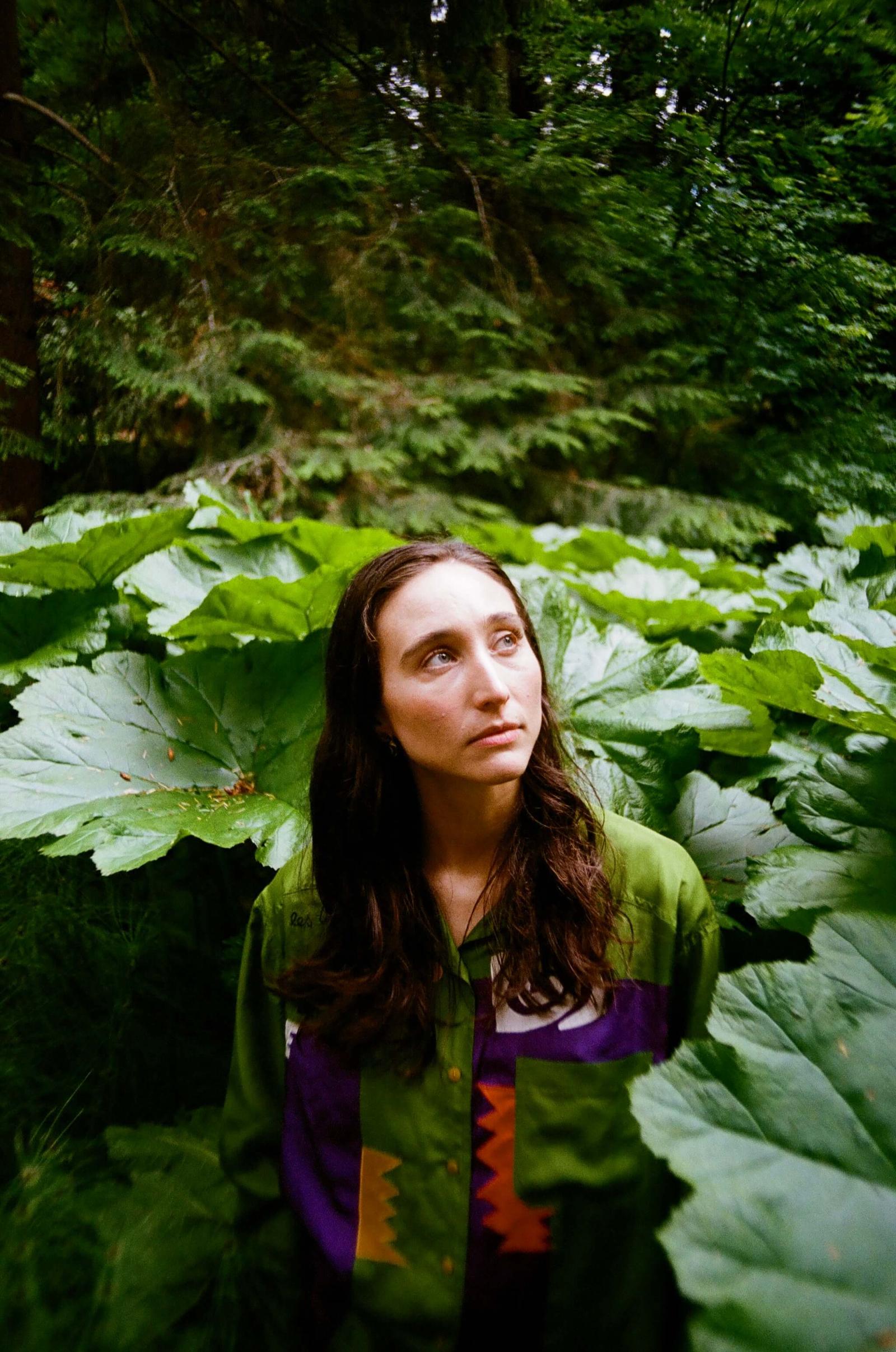 abbey blackwell in a green lush forrest in a green sweater with long brown hair