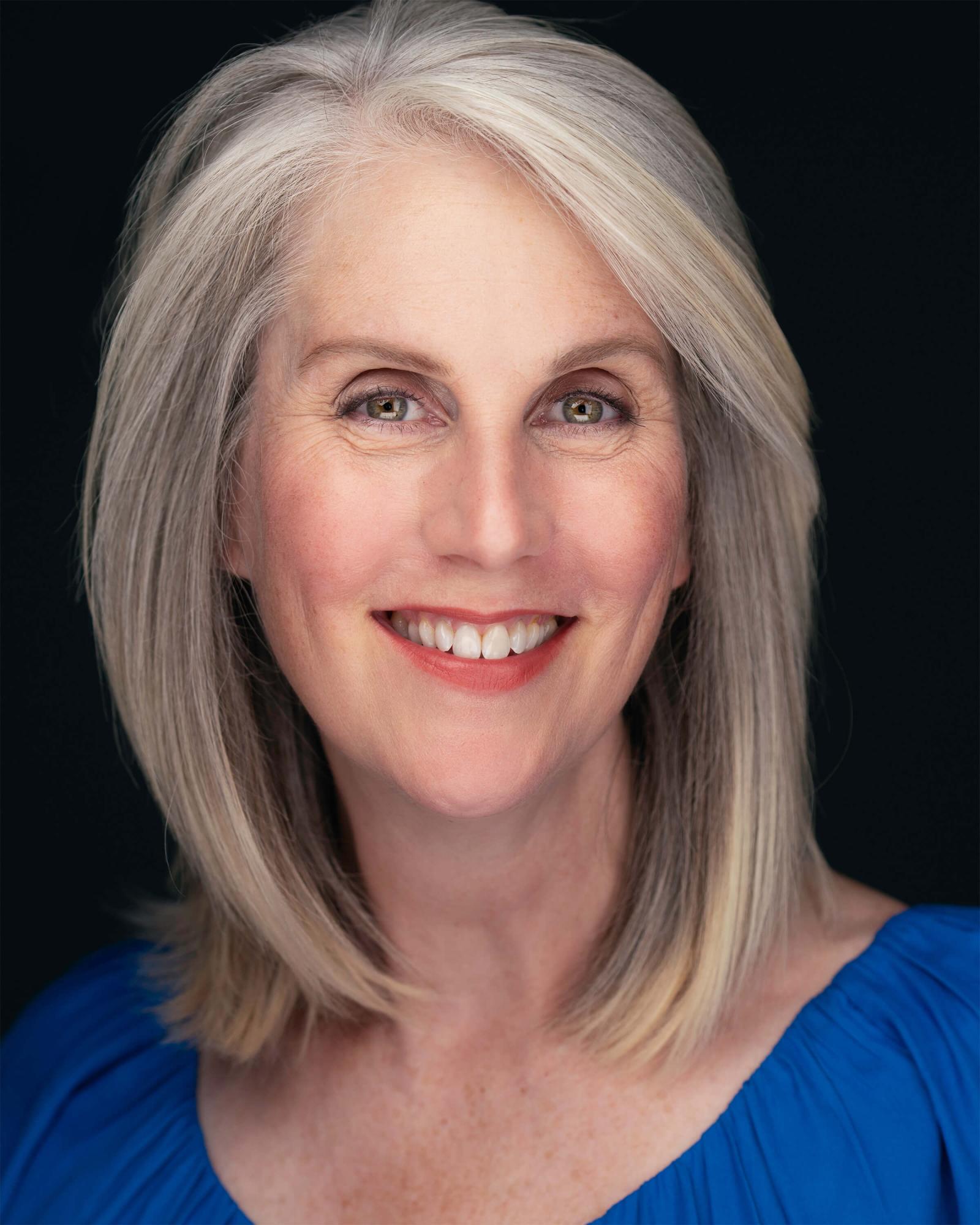 Nikki Visel headshot in a blue shirt with gray hair. 
